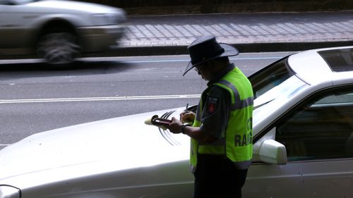 A parking inspector issues a ticket to a car parked on Macquarie Street in Sydney's CBD.