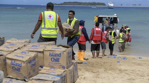 In this photo provided by Malau Media/IFRC, Tonga Red Cross Society's staff and volunteers unloading boxes of water bottles from the boat into the beach in Nomuka Ha'apai Island, Tonga on April 1, 2022. Three months on from a devastating volcano and tsunami in Tonga, the AP checks in on how the island nation is recovering. The bill from the tsunami is estimated at some $90 million and GDP is expected to fall by more than 7% this year. The cleanup has been hindered by an internet outage caused by