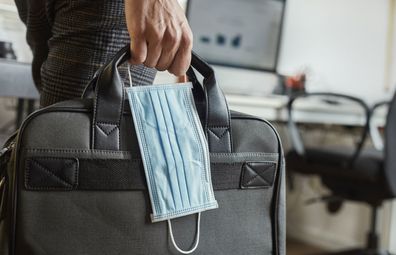 Office worker carrying laptop and coronavirus mask