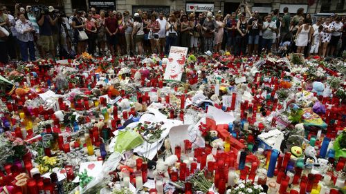 People stand next to candles and flowers placed on the ground after a terror attack in Barcelona. (AAP)