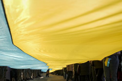 A child walks under a large Ukrainian flag carried by people marking a "day of unity" in Sievierodonetsk, the Luhansk region, eastern Ukraine, Wednesday, Feb. 16, 2022. 
