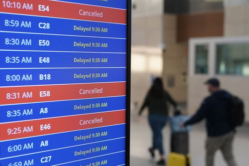 Travellers walk as a video board shows flight delays and cancellations at Ronald Reagan Washington National Airport in Arlington, Va., Wednesday, Jan. 11, 2023.