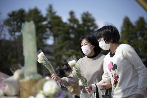 Visitors offer flowers at a makeshift altar to mourn for the victims of the March 11, 2011 earthquake and tsunami during a special memorial event Friday, March 11, 2022, in Tokyo, Japan.