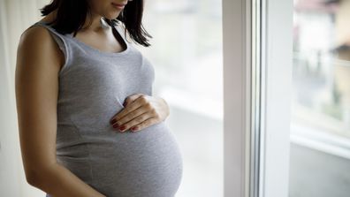 Portrait of young pregnant woman standing by the window