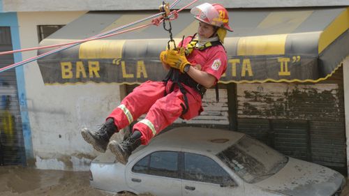 A rescuer zip-lines past a bogged car. (AFP)
