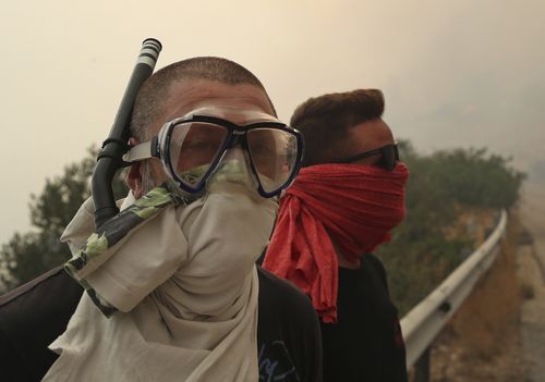 People cover their faces - and one adopts a snorkel - to beat the smoke. Picture: AP