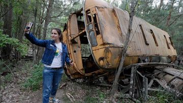 A visitor takes a selfie with an abandoned bus during a tour in Chernobyl.