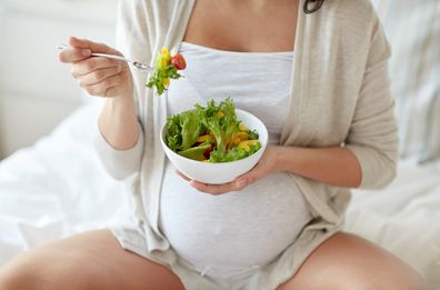 pregnant woman eating vegetable salad in bed at home