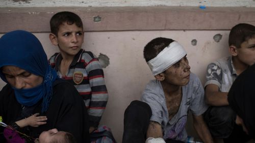 Iraqi civilians sit inside a house as they wait to be taken out of the Old City during fighting. (AAP)