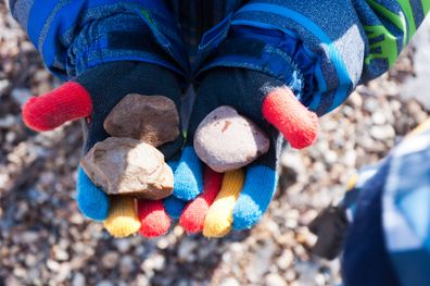 A boy in multi-colored gloves holds three stones.