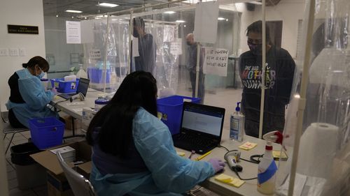 Administrative workers Leslie Castillo, far left, and Veronica Esparza check in people at a COVID-19 testing site in Los Angeles.