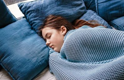 Young teenager girl sleeping snuggled in warm knitted blue blanket. Seasonal melancholy, apathy and winter blues. Cozy home.