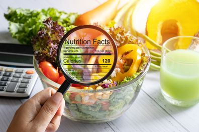 Nutrition information concept.Hand zooming in with a magnifying glass to view nutrition facts details of food, salad bowl