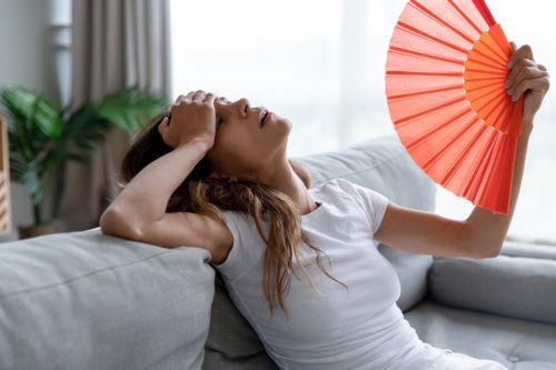 Girl using paper fan, suffering from hot summer weather or high temperature at home. 