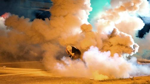 A protester seeks cover from a smoke grenade. (AAP)