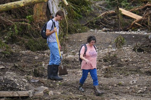 People walk along debris near the banks of the Guadalupe River after a flash flood swept through the area Saturday, July 5, 2025, in Hunt, Texas. (AP Photo/Julio Cortez)