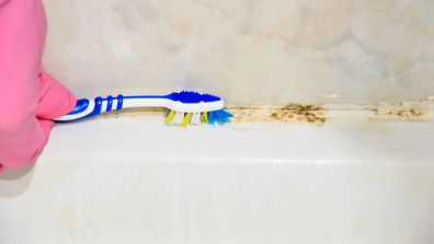 Cleaning moldy tile with a toothbrush at bathroom