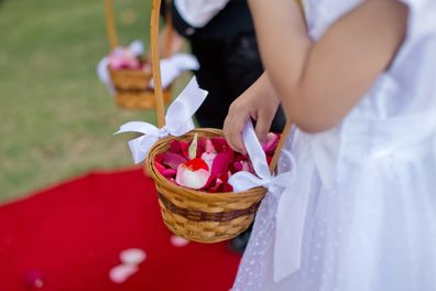 Small flower girl and boy hands holding flower hanging basket at an outdoor wedding