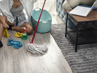 Woman cleaning floor while husband works on lounge