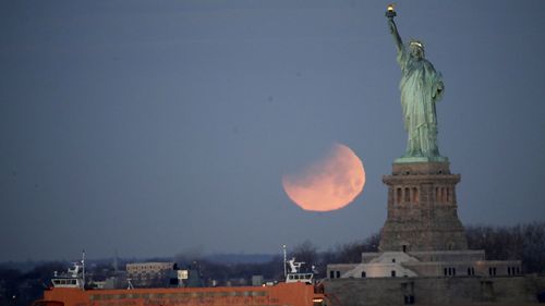 The Statue of Liberty and the Staten Island Ferry are backdropped by a supermoon. (AAP)