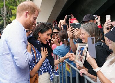 A well-wisher presents Prince Harry, Duke of Sussex, with a framed photo of him with her mother Daphne Dunn, as he arrives with Meghan, Duchess of Sussex at the Man O'War Steps, next to the Sydney Opera House, before taking part in a sailing event with members of Invictus Australia in Sydney Harbour, on day four of the royal tour on April 17, 2026 in Sydney, Australia. The royal couple are on a four-day visit to Australia, with engagements in Melbourne, Canberra and Syd