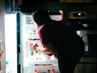 A pregnant woman is getting into the kitchen refrigerator at midnight to get a snack. Giving into her pregnancy cravings.