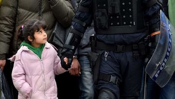 A police officer walks hand in hand with a young girl across Croatia's border with Slovenia. (Getty)
