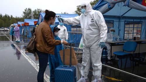 A worker in protective overalls take the temperature of a traveller from Wuhan in April