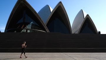A woman walking in front of a nearly deserted Sydney Opera House. Sydney is seeing a dramatic reduction in people on the streets as people are asked to enact social distancing and self isolation in order to prevent the spread of Covid-19.