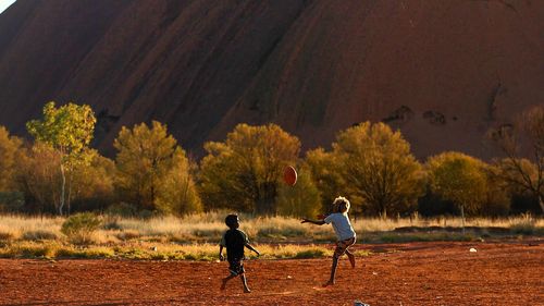 Local children play a scrappy game of football on a dusty field in the shadow of Uluru.