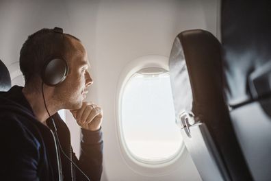 Traveling man on airplane flying charter.  Using smartphone and using noise-cancelling headphones
