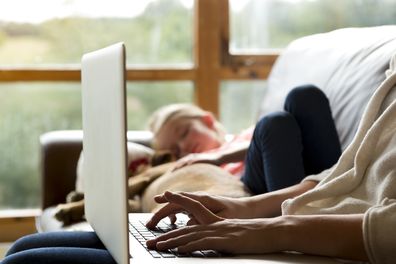 Woman using a laptop with her daughter and pet dog sleeping together next to her