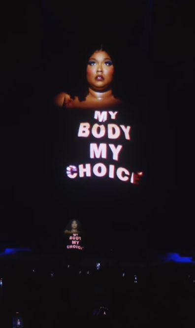 Lizzo responds to Kanye West's comments about her body on stage by projecting the words "My body my choice" onto her.