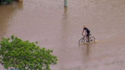 Man rides his bike through flood waters