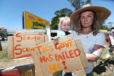 Tuntable Falls resident Amanda Collien and her daughter Etienne, 2 hold up hand-painted signs in the bushfire affected area of Nimbin, NSW, Tuesday, November 12, 2019. (AAP Image/Jason O'Brien) NO ARCHIVING
