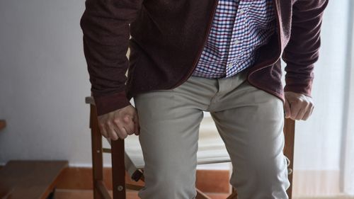 Horizontal photo. Selective blur. A mature man has difficulty getting up from an armchair in the living room of his home.