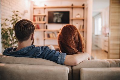 Back view of relaxed couple watching a movie on TV in the living room