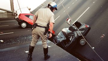 In this 1989 file photo, a California Highway Patrol officer checks the damage to cars that fell when the upper deck of the Bay Bridge collapsed onto the lower deck after the Loma Prieta earthquake in San Francisco. 