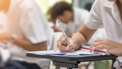 Exam at school with student's taking educational admission test in class, thinking hard, writing answer in university classroom, education and world literacy day concept