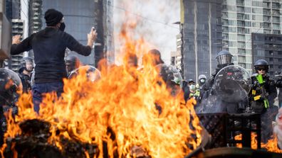 MELBOURNE, AUSTRALIA - SEPTEMBER 11: A protester stands in front of police officers as rubbish bins burn on Spencer Street on September 11, 2024 in Melbourne, Australia. Anti-war protesters in Melbourne are planning to disrupt the upcoming Land Forces International Defence Expo by blocking streets and staging peaceful demonstrations, with estimates of up to 25,000 participants. Activist groups, including Students for Palestine and Disrupt Wars, aim to obstruct the expo's opening on Wednesday, cl