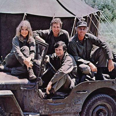 Alan Alda in the driving seat of a jeep, surrounded by Loretta Swit and other cast members of the hit television show M.A.S.H.