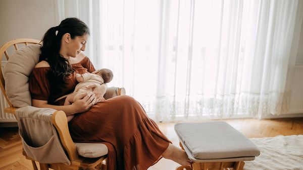 Brunette women sits on a chair holding newborn baby.