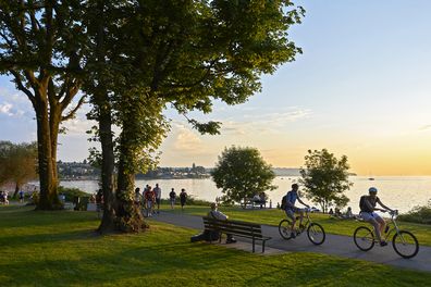 Vancouver, B.C., Canada - July 18, 2012: Young couple cycling, others walking or jogging late afternoon and enjoying the sunset at Stanley Park