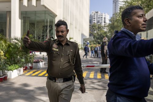 Un policier et un agent de sécurité privé demandent aux journalistes de sortir de la porte d'un immeuble abritant le bureau de la BBC à New Delhi, en Inde, le mardi 14 février 2023. 