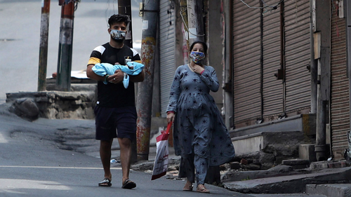 Indians wearing face masks as a precaution against the coronavirus walk past closed market during reimposed weekends lockdown to prevent the spread of new coronavirus in Jammu, India, Sunday, July.26, 2020.(AP Photo/Channi Anand)