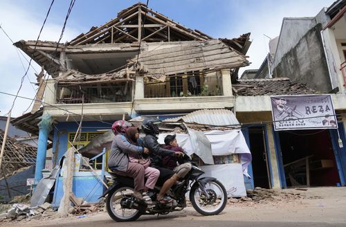 Люди едут на мотоцикле перед зданием, пострадавшим в результате землетрясения в понедельник в Чианджуре, Западная Ява, Индонезия, вторник, 22 ноября 2022 года. несколько из них.  человек и сотни получили ранения на главном острове Ява в Индонезии.  (AP Photo/Татан Сюфлана)