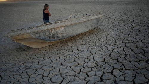 Misha McBride looks at a formerly sunken boat now on cracked earth hundreds of feet from what is now the shoreline on Lake Mead at the Lake Mead National Recreation Area.