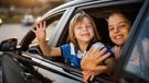 Two children wave through open windows of a car.