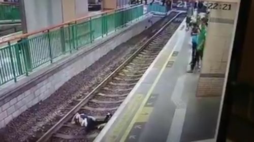 As the woman lies motionless on the tracks, the man walks away calmly. (Facebook)