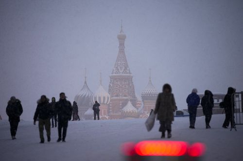 People walk through Red Square during a snowfall, with St. Basil's Cathedral, center, and the Mausoleum of the Soviet founder Vladimir Lenin, right, in the background in Moscow, Russia, Monday, Jan. 31, 2022. (AP Photo/Alexander Zemlianichenko)